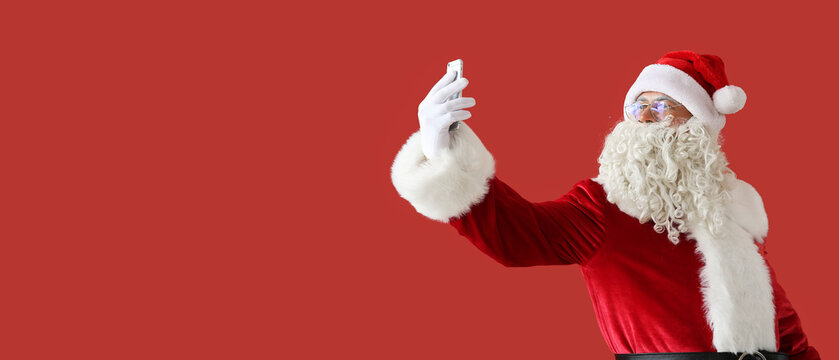 Portrait of Santa Claus with mobile phone taking selfie on red background with space for text