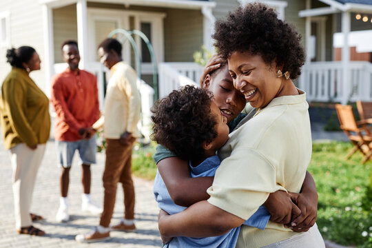 Portrait of smiling black woman embracing two sons at family gathering outdoors, copy space