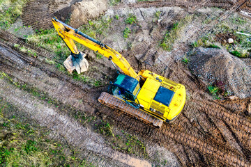 A powerful excavator digs the ground at a construction site. View from above. Drone photography. Earthworks with heavy equipment at the construction site.