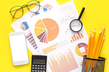 Business charts, mobile phone and stationery on yellow background