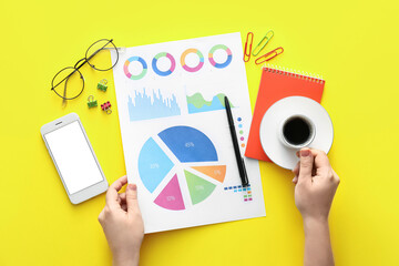 Female hands with business charts, mobile phone and stationery on yellow background