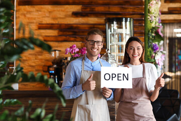 Business owners with opening sign showing thumbs-up in their cafe
