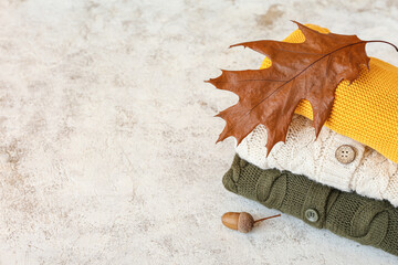 Stack of different children's sweaters, acorn and autumn leaf on grunge background