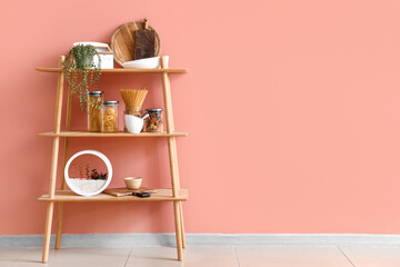 Shelving unit with food, houseplant and kitchen utensils near pink wall