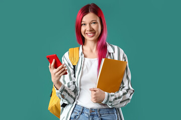 Young female student with bright unusual hair holding phone on green background