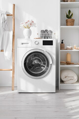 Modern washing machine and shelf unit with bath accessories near white wall