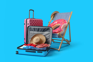 Deck chair, suitcases and beach accessories on light blue background