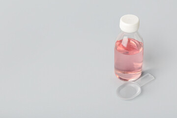 Bottle of cough syrup and spoon on grey background