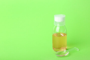 Bottle and spoon of cough syrup on green background