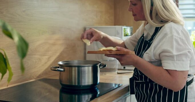 Woman in beautiful apron standing in modern kitchen holding desk with tasty gnocchi pierogi varennyki dumplings putting in boiled water cooking process concept.