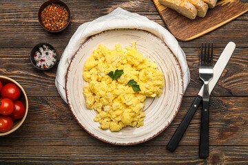 Plate of tasty scrambled eggs, tomatoes and spices on wooden background