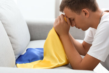 Young man with flag of Ukraine praying at home