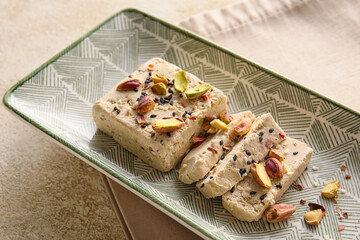 Plate of tasty sesame halva with pistachios on light background, closeup
