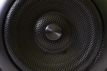 The central fragment of a modern audio speaker with a protective black metal grille. Macro.