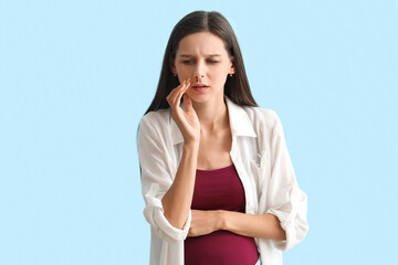Young pregnant woman with nosebleed on blue background