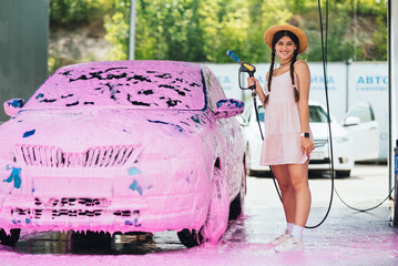 Woman with hose stands by car covered in pink foam