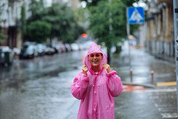 Young smiling woman with raincoat while enjoying a rainy day. - 537711257
