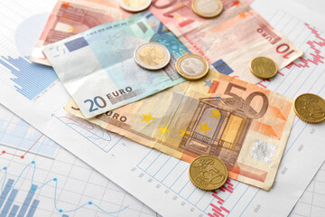 Euro banknotes with coins on diagrams, closeup. Exchange rate concept