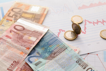 Euro banknotes with coins on diagrams, closeup. Exchange rate concept