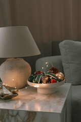Christmas decorations in ceramic vase, modern lamp on marble table. Cozy evening home atmosphere. 