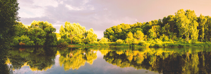 Summer sunset scene with calm forest pond and green trees