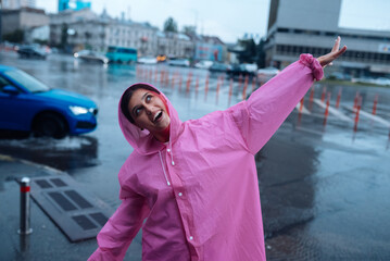 Obraz premium Young smiling woman in a pink raincoat enjoying a rainy day.