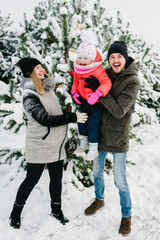 Happy family near decorated Christmas tree having fun in a winter forest. Mom, dad and daughter...