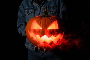 Close-up of glowing halloween pumpkin with smoking mouth and eyes on dark.