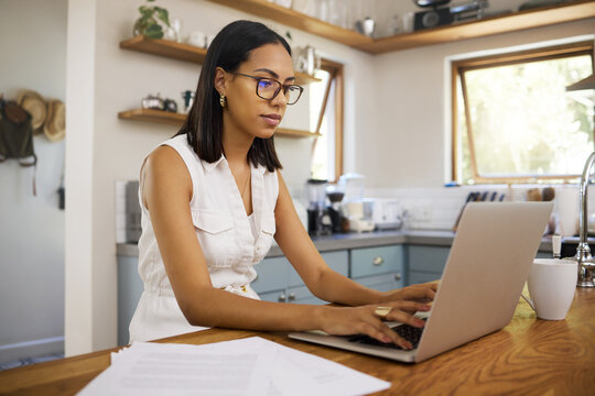 Woman in business, working on laptop from home and sitting in a kitchen with contract documents on table. Freelance accounting entrepreneur, remote work in house and finance paperwork use 5g internet