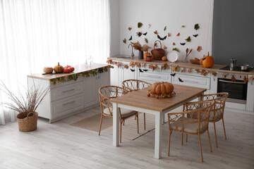 Interior of modern kitchen decorated for Halloween with pumpkins, dining table and white counters