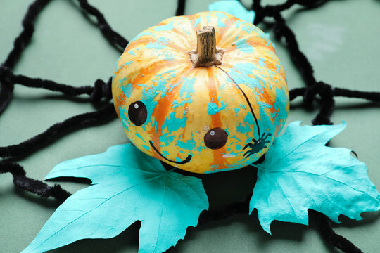 Halloween pumpkin, leaves and spider web on color background, closeup