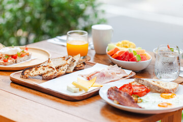 Healthy breakfast with eggs, bacon and ham in outdoors hotel cafe. Lunch served with orange juice, toast, cheese and fruits. Balanced diet