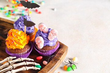 Board with tasty Halloween cupcakes and decor on white background