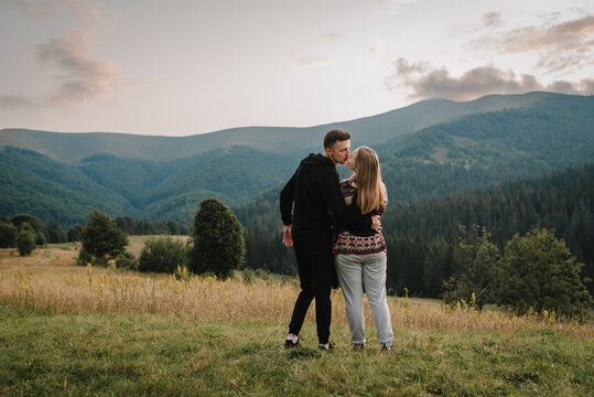 Young couple hugging and kissing, at sunset in autumn. A man and a woman stand on the grass in the field and enjoy the nature of the mountains. Concept of friendly family. Place for text and design.
