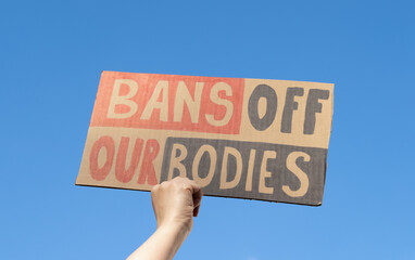 Woman hand holding placard sign with slogan Bans Off Our Bodies during manifestation. Female...