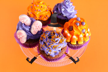 Fototapeta premium Stand with tasty Halloween cupcakes on orange background, closeup