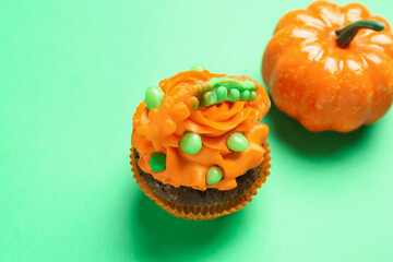 Tasty Halloween cupcake and pumpkin on green background, closeup