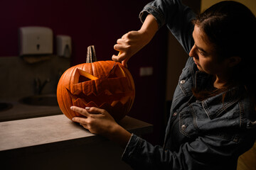woman accurate carving orange pumpkin for Halloween and making scary face on jack-o-lantern