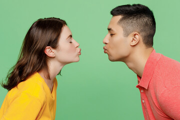 Side view close up caucasian young couple two friends family man woman 20s wear basic t-shirts together going to kiss each other isolated on pastel plain light green color background studio portrait.