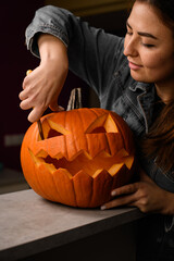 woman carving orange pumpkin for Halloween and making scary face on jack-o-lantern