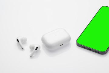 Wireless headphones lie on a white table, white background, smartphone screen chromakey.