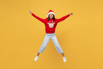 Fototapeta na wymiar Merry little kid teen girl 13-14 years old wear red xmas sweater with deer Santa hat posing jump high with outstretched hands isolated on plain yellow background. Happy New Year 2023 holiday concept.
