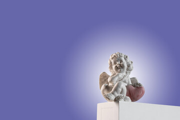 Figurine of an angel Cupid on the podium with a red heart on a very peri purple background ....