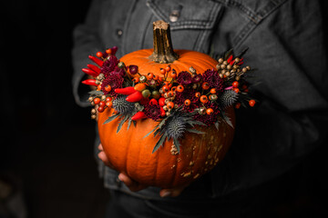 lovely autumn arrangement of flowers berries and pepper in pumpkin on hands of woman.
