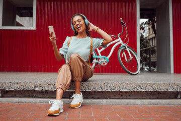 Happy woman, phone and headphones for music or listening to podcast while sitting on a urban city...
