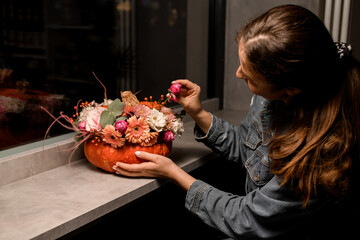 female florist accurate decorates flower arrangement of fresh roses and other flowers in orange...