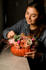 woman florist accurate decorates flower arrangement of fresh roses and other flowers in orange pumpkin. Autumn bouquet