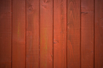 Photo of a wooden wall of a country house. The background is made of wood painted with rowan-colored paint. Fence made of red boards