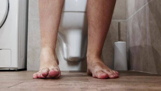 A man puts on denim shorts in the toilet after having a bowel movement. Koznept prolonged sitting on the toilet. Health of the intestines and digestive tract, hemorrhoids.