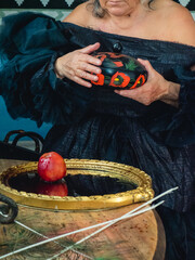 senior woman dark witch gypsy character making witchery spell on apple with blood in mirror -...